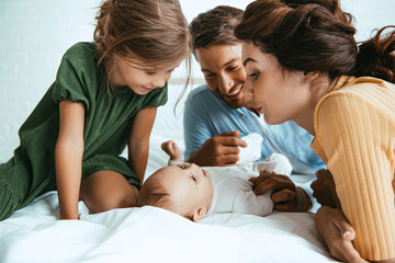 Wall Mural - happy family looking at adorable infant lying on white bedding