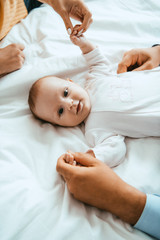 Wall Mural - top view of mother and dad playing with smiling baby lying on white bedding