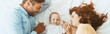 © LIGHTFIELD STUDIOS - panoramic shot of happy parents gently touching adorable baby while lying on white bedding together