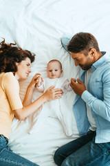 Wall Mural - happy parents gently touching adorable baby while lying on white bedding together