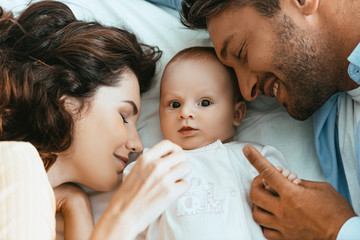 Wall Mural - happy mother and father lying near adorable infant with closed eyes