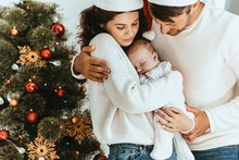 Happy Father Embracing Wife Holding Cute Baby Near Christmas Tree