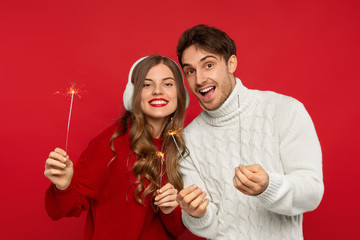 happy young couple holding Christmas sparklers isolated on red background. Christmas concept