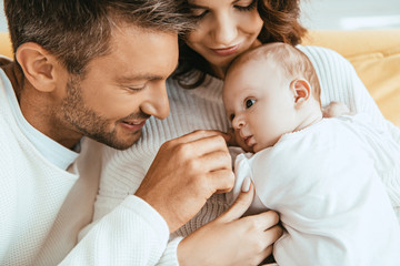 Wall Mural - happy father touching adorable little daughter lying on mothers hands