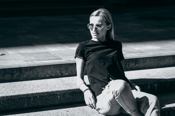 Wall Mural - Girl wearing black t-shirt, glasses and leather jacket posing against street , urban clothing style. Street photography