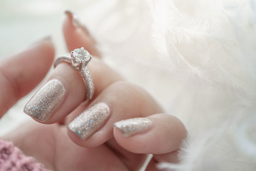 Wall Mural - Close up of diamond ring on woman's finger with pink sweater and white feather. (soft and selective focus) love and wedding concept.