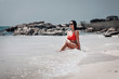 © Semachkovsky  - Attractive lady in red bikini and sunglasses sits on the beach in the tidal waves, relaxation concept.