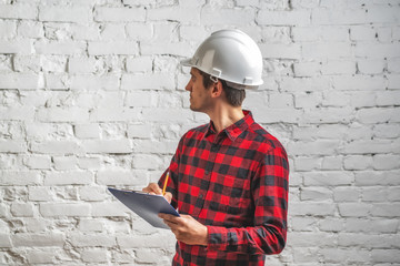 a civil engineer in a white helmet examines documents against a white brick wall. Preparation for finishing