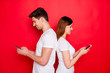 © deagreez - Photo of girlfriend boyfriend standing back to back chatting to each other browsing through telephone smiling toothily wearing white t-shirt isolated vivid color background