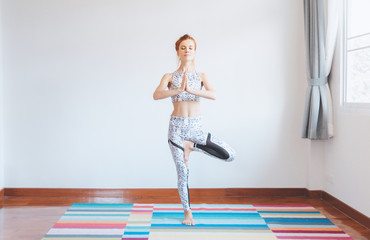 Smilling young caucasian woman practic yoga  ,standing tree pose on mat in the morning at home, calm, peace , mingful .Yoga concept, Healthy work life balance.