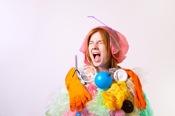 Emotional redhead woman looking stressed, covered with eco harmful plastic garbage, bags and straws of different color. Zero waste concept. Sad female frowning, angry about littering.