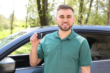 Young man with key near new car outdoors