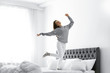 © New Africa - Young woman in warm sweater jumping on bed at home