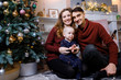 © antonkorobkov - Beautiful young family sits on a carpet near the fireplace next to a large elegant Christmas tree