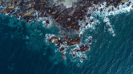 Aerial view of the coastal edge with waves, rocks and white foam