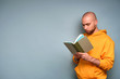 © bestsenny - A guy with a beard in a yellow sweatshirt stands on a blue background in a half-turn and looks in a green book