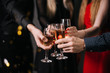 © dikushin - Close-up of man and woman hands clinking with champagne glasses. Four beautiful and cheerful friends in festive clothes on background.