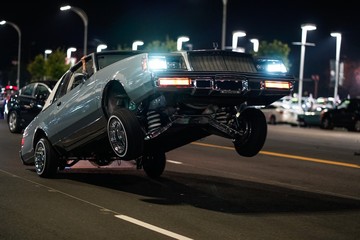 Wall Mural - Closeup shot of a retro car with only the back wheels on the ground in a street at night