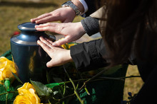 Three Hands Touching A Cremation Urn At A Funeral