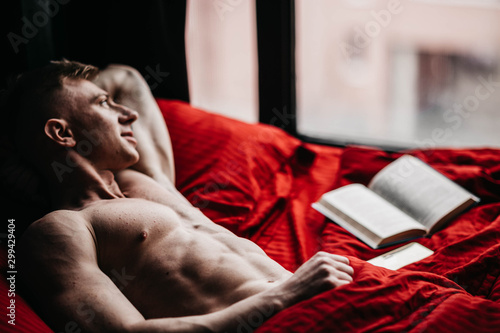 Cuadros en Lienzo Sexy young man in bed is reading a book. A handsome intellectual.