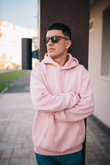 Wall Mural - City portrait of handsome hipster guy wearing pink blank hoodie or hoody with space for your logo or design. Mockup for print