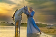 blonde with a horse near the water at sunset