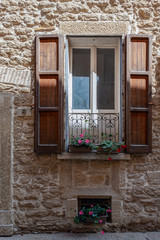 Wall Mural - Picturesque window of an old building with wooden shutters, a metal balcony and potted flowers