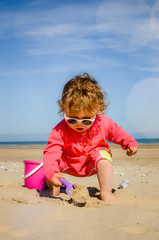 Canvas Print - pretty little girl playing on the beach and protected from the sun