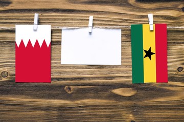 Hanging flags of Bahrain and Ghana attached to rope with clothes pins with copy space on white note paper on wooden background.Diplomatic relations between countries.