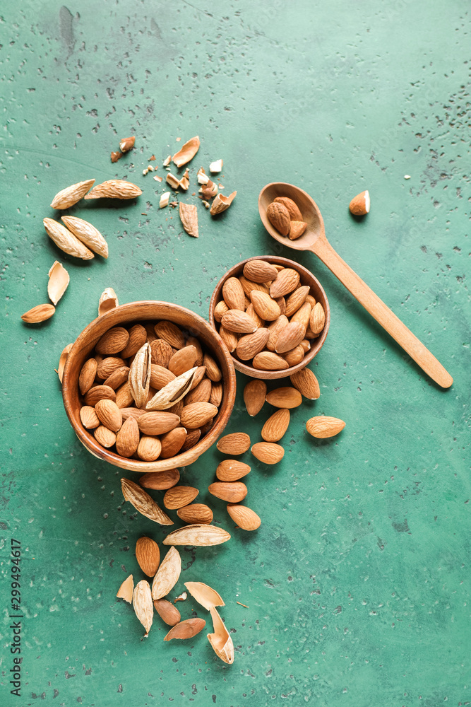 Bowls with tasty almonds on color background