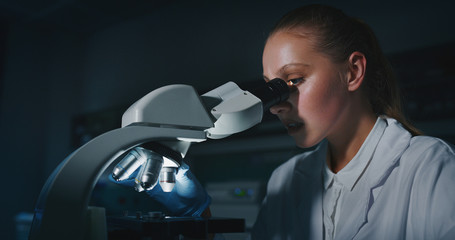 Portrait of blond female scientist is analyzing a sample to extract the DNA and molecules with microscope in laboratory.