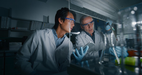 Portrait of two male scientists are making an analysis of the DNA and molecules in the test tubes and signs results in laboratory.