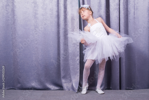 Obraz Dibond Little cute girl in a white dress on the background of theatrical curtains.