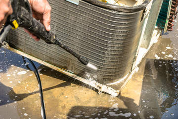 a professional electrician is cleaning the window air conditioner on the roof top of a house with his high pressure water gun   