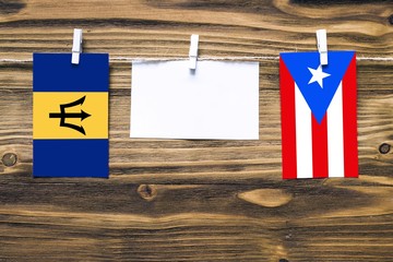 Hanging flags of Barbados and Puerto Rico attached to rope with clothes pins with copy space on white note paper on wooden background.Diplomatic relations between countries.