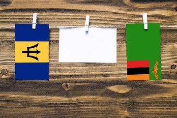 Hanging flags of Barbados and Zambia attached to rope with clothes pins with copy space on white note paper on wooden background.Diplomatic relations between countries.
