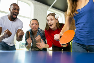 Wall Mural - Young people playing table tennis in workplace, having fun. Friends in casual clothes play ping pong together at sunny day. Concept of leisure activity, sport, friendship, teambuilding, teamwork.