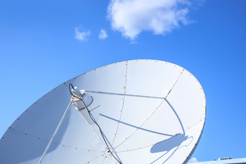 White big parabolic satellite antenna for telecommunications on a background of blue sky.