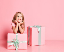 Christmas And New Year. Nice Kid Girl Sitting Behind Gifts Boxes With Her Chin In Her Hands Dreaming, Waiting On Pink