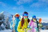 Men and woman with snowboard and skis standing on snow resort against backdrop of mountain.