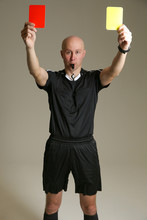 Bald Football Referee On Gray Background. Soccer Referee Raised Both Cards Up. Football Referee In A Black Uniform Holding A Red And Yellow Card. The Soccer Referee Shows Two Cards At Once.