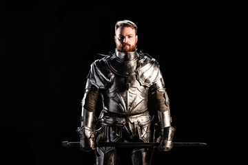 handsome knight in armor holding sword isolated on black