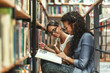 © BalanceFormCreative - Two female students reads a book by the bookshelf at the library. Reading a book.