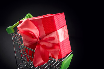 Present gift box in festive packaging with satin bow in the shopping basket. Delivery of gifts by the postal cargo service or from the online store. Concept of New Year, birthday, preparation.