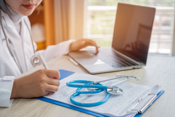 Wall Mural - Medicine doctor writing document file for patient at consulting room, working on laptop computer on desk in clinic, stethoscope on foreground table in hostpital. Healthcare and medical concept.