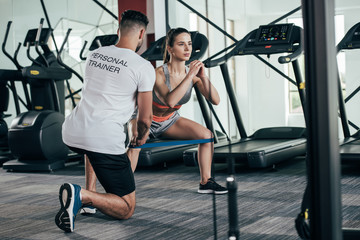 Wall Mural - back view of personal trainer supervising young sportswoman exercising with resistance band