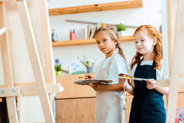 selective focus of cheerful kids with multicolored palette near canvas