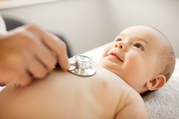 medicine, healthcare and pediatrics concept - close up of female doctor with stethoscope listening to baby girl's patient heartbeat or breath at clinic or hospital