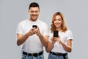 Wall Mural - technology and people concept - happy couple in white t-shirts with smartphones over grey background