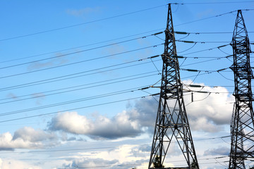 Towers of electric main with the wires against the blue sky with clouds. High voltage lines and power pylons.Transformer with high-voltage wires technogenic landscape, high-voltage power lines.